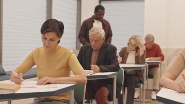 Sınıfta erkek siyah koçla ders çalışan bir grup olgun erkek ve kadın test ya da muayene oluyorlar.
