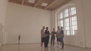 Aktif giyimli, ellerinde yoga minderleri olan ve genç ve fit yoga hocaları parlak geniş yoga stüdyosunda sohbet eden geniş bir grup son sınıf öğrencisi.