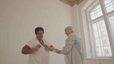 Geniş dans stüdyosunda dans ederken eğlenen dört aktif çok ırklı yaşlının görüntüsünü büyüt.