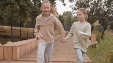 Yazın parkta el ele tutuşarak kameraya doğru koşan 10 yaşındaki Kafkas kızlarının yavaşlaması.