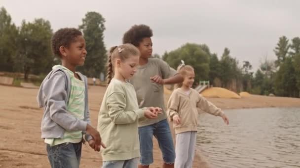 Kumsalda Göle Taş Atarken Birlikte Eğlenen Dört Neşeli Çokkültürlü Çocuğun — Stok video