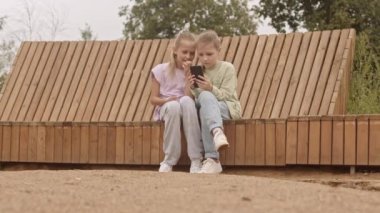 Dört farklı okul arkadaşının yazın açık havada ahşap bankta otururken akıllı telefon kullanması.