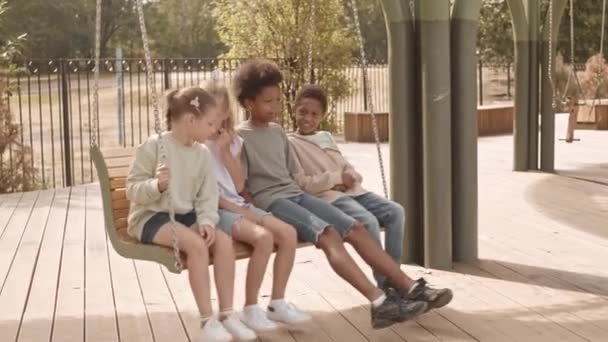 Slowmo Four Cheerful Multiethnic Kids Talking While Swinging Wooden Swing — Stock Video