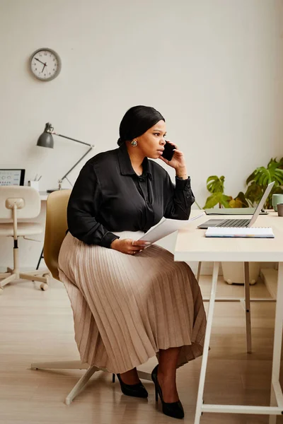 小規模オフィス内の職場でスマートフォンでクライアントを呼び出すエレガントな黒のビジネス女性の完全な長さの肖像画 — ストック写真
