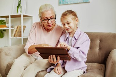 Samimi evde dijital tablet ve internet kullanarak büyükanneme öğretmenlik yapan gülümseyen küçük kızın portresi.