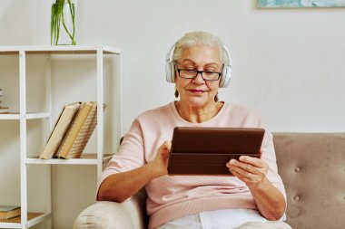 Modern son sınıf öğrencisi kadının portresi, minimumda otururken kulaklıkla dijital tablet kullanıyor.