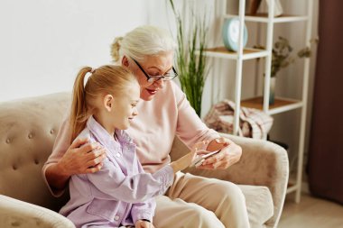 Büyükannesine cep telefonunu gösteren ve interneti öğreten gülümseyen küçük kızın yan görünümü.