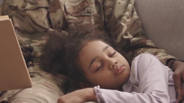 一个身穿军服 面目全非的黑人女子慢吞吞地给她漂亮的小女儿读书 在家里的沙发上打盹 — 图库视频影像