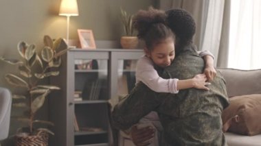 Uzun bir görevden sonra evine dönen ve 6 yaşındaki kızını şefkatle kucaklayan Afrika kökenli, asker üniformalı genç bir Amerikan subayı.