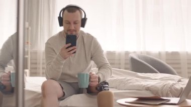 Normal giyimli, kulaklıklı, protez bacaklı bir gencin evinde yatağında kahve ya da elinde çayla arkadaşlarıyla mesajlaşması.