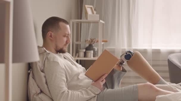 의족을 착용하고 주말을 집에서 침대에서 읽으면서 보내는 집중적 젊은이의 — 비디오