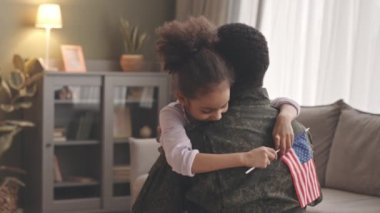 Amerikan bayrağı elinde, uzun bir ayrılıktan evine dönen askerî babasına sarılıp koşan mutlu Afrikalı Amerikalı küçük bir kız.