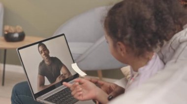 Bilgisayarda asker babasıyla görüntülü sohbet ederken annesinin kucağında oturan Afrikalı Amerikalı kızın yavaş çekimleri.