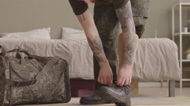 Uzun bir görev için evden ayrılmadan önce ayakkabı bağcıklarını bağlayan askeri üniformalı, protez bacaklı düşük rütbeli bir asker.