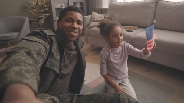 手持Pov慢镜头的年轻的身穿军服的非洲裔美国军官和手持美国国旗的漂亮小女儿在家里拍照时对着镜头微笑 — 图库视频影像
