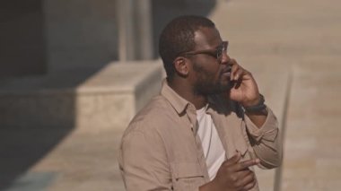 Koyu gölgeli siyah adamın belini kaldır güneşli bir günde açık havada akıllı telefondan konuşuyor.