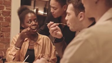 Eşcinsel arkadaşlarıyla akşam yemeği yiyip, şarap içip sohbet ederken Afrikalı Amerikalı sevgilisini yanağından öpen melez bir kadın.