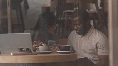 Kafe masasında yan yana otururken iş projelerini tartışan genç, güzel esmer kadın ve Afrikalı Amerikalı erkek arkadaşının orta yavaşlığı.