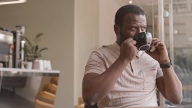 Akıllı telefonla konuşurken kapuçino yudumlayan, ofisinin yakınındaki kahve dükkanında çalışan, gülümseyen genç Afrikalı Amerikalı iş adamının yavaşlığı.