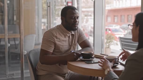 中等速度慢的非裔美国商人倾听女性商业伙伴的声音 在阳光灿烂的日子里一起坐在茶几旁喝咖啡 — 图库视频影像