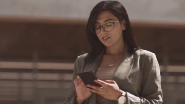 Düşük açılı orta yaşlı, çekici, çift ırklı iş kadını, koyu renk düz saçlı, şık gözlüklü, güneşli bir günde açık havada telefonla konuşan.