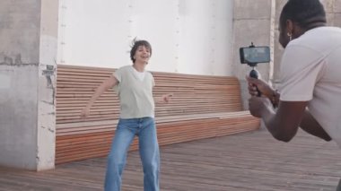 Enerjik genç bir kadın açık havada dans ediyor ve Afrika kökenli Amerikalı erkek arkadaşı akıllı telefon kamerasıyla dansını kaydediyor. Hem eğleniyor hem de eğleniyor.