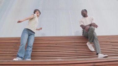 Düşük açılı, çok ırklı, aktif, genç bir çift bankta dans ederken eğleniyor.