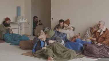 Soğuk akıl hastanesinde birlikte yaşayan ve hayatta kalmak için birbirlerine destek olmaya çalışan giysi ve uyku tulumu giymiş genç ve yetişkin kadın ve erkek gruplarının yavaşlaması.