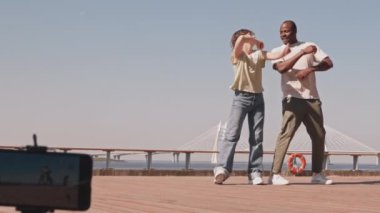 Genç ve çeşitli blogcuların tam boy yavaşlığı. Güneşli bir günde akıllı telefonlarıyla dans ederken videolar kaydediyorlar.