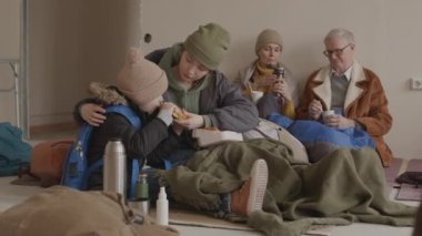 Diğer mültecilerle birlikte soğuk sığınma evinde kalırken 7 yaşındaki oğlunu sandviçle besleyen Kafkasyalı genç kadın yavaşlıyor.