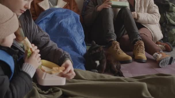 寒い避難所で一緒に暮らす小さな息子とホームレスの黒い猫を持つ若い女性を含む多様な難民の作物の減速 食糧と水を供給 — ストック動画