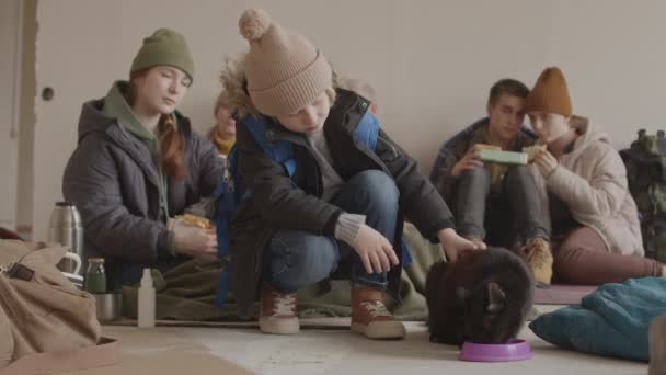 寒い避難所で母親や他の難民の人々と一緒に住んでいる間 7歳の男の子の遅いペットホームレスの黒い猫 — ストック動画