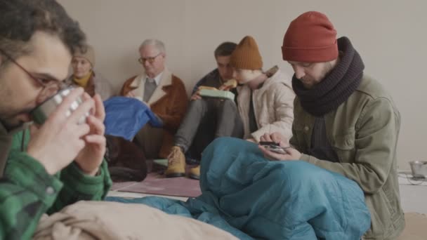用手机与家人联系 然后悲伤地看着与其他难民坐在冷藏室地板上的相机的慢幅肖像 — 图库视频影像