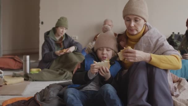 许多无家可归的成年妇女一边吃着食物 一边抱着自己的小儿子 坐在简陋的难民收容所地板上 — 图库视频影像
