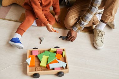 Siyah baba ve oğlunun çocuk odasında yerde oturup tahta oyuncaklarla oynadığı yakın plan çekimleri.