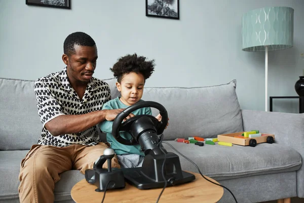 Portrait of black father and son playing racing games on PC with steering wheel, copy space