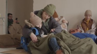 Diğer mültecilerle birlikte soğuk bir sığınakta oturan, gidecek hiçbir yeri olmayan, 7 yaşındaki oğlunu kucaklayan, umursamaz, genç, beyaz bir kadın.