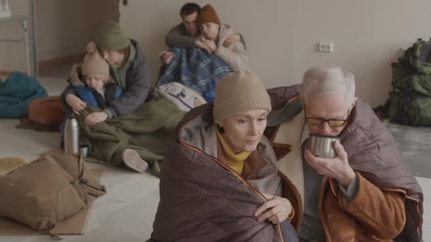 寒い避難所に住む難民男性と女性の小さなグループのスローモは 暖かい服や寝袋を提供します — ストック動画