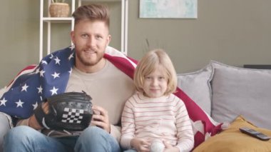 Omuzlarında Amerikan bayrağı, ellerinde beyzbol eldiveni ve elinde topla evlerinde heyecanlı bir maç izleyen, takım için tezahürat yapan Kafkasyalı genç bir adam ve 7 yaşındaki oğlunun POV yavaşlaması.