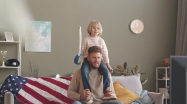 7 yaşında, elinde oyuncak kılıcıyla babasının omuzlarında oturan, televizyonda heyecanlı bir film ya da spor maçı izleyen beyaz bir çocuk.