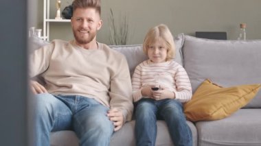 Beyazların babası ve 7 yaşındaki oğlu, oturma odasındaki kanepede otururken spor maçı izliyorlar ve takımları kazanırken ellerini havaya kaldırıyorlar.