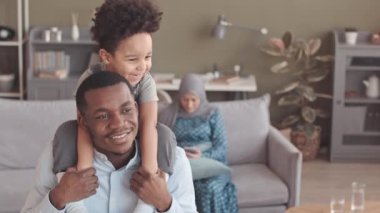 Afrikalı Müslüman bir babanın yavaş portresi ve 3 yaşındaki oğlu kameraya gülümserken tesettürlü çocuklar arka plandaki koltukta oturan akıllı telefonlu anneler