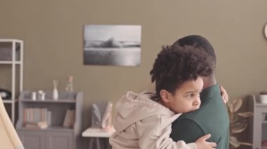 Afrika kökenli Amerikalı bir adamın kucağında taşıdığı ve kucağına aldığı çocuk modern oturma odasında zeytin yeşili duvarlarla dikiliyor.