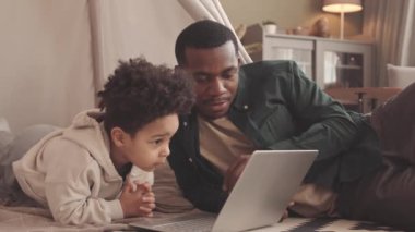 Haftasonunu evde birlikte geçirirken dizüstü bilgisayarında çizgi film izleyen Afrikalı genç bir adam ve küçük tatlı oğlu.