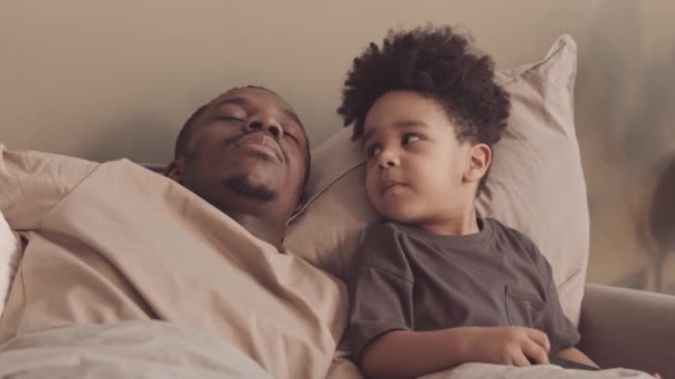 午後に幼児の息子とテレビを見ている間 アフリカ系アメリカ人のシングルファーザーの遅い昼寝 かわいい男の子は彼を起こそうとしている — ストック動画