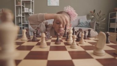 Evde satranç oynayan, hareketlerini ve kombinasyonlarını düşünen akıllı 8 yaşındaki kız.
