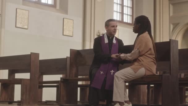 若いアフリカ系アメリカ人の女性のスローモ黒と紫のローブで成熟した白人の司祭と話を 一緒に木の泥を保持手に座って — ストック動画