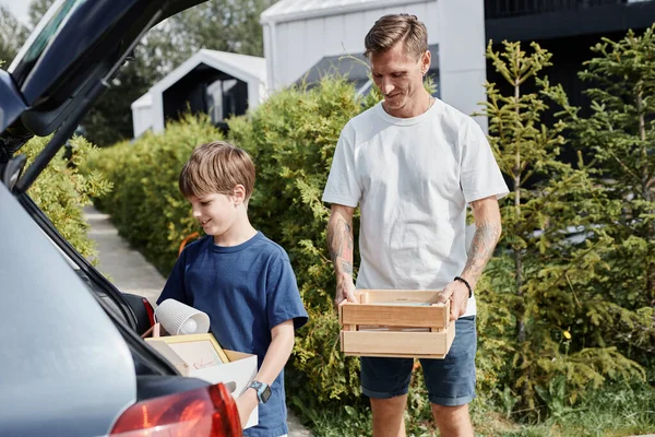 Portrait of father and son carrying boxes to car while moving into new house, copy space