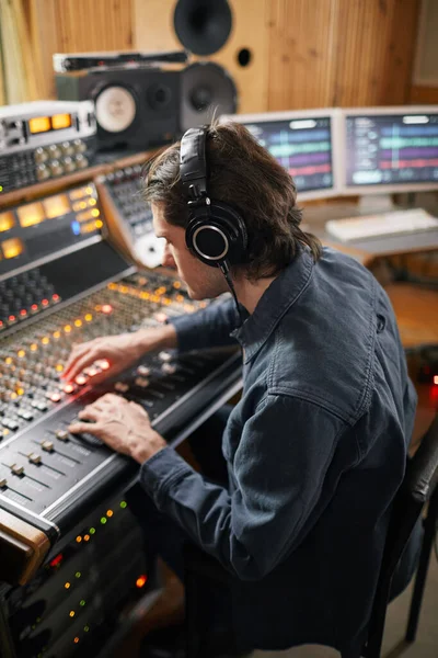 録音スタジオのオーディオワークステーションでヘッドフォンを身に着けている男のサイドビューの肖像画 音楽制作のテーマ — ストック写真