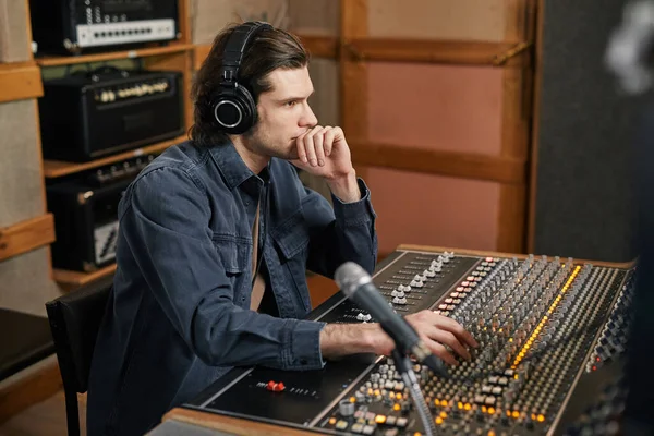 stock image Side view portrait of focused young man wearing headphones at audio workstation in professional recording studio, music production and artistry